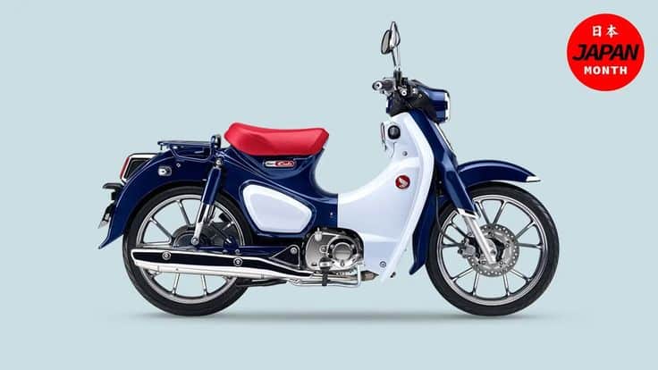 Classic blue and white motorcycle with a red seat, showcasing vintage design. Japan Month promotion badge visible.