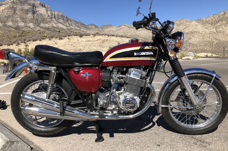 Red Honda motorcycle parked in desert landscape, showcasing classic design and chrome details. Perfect for vintage bike enthusiasts.