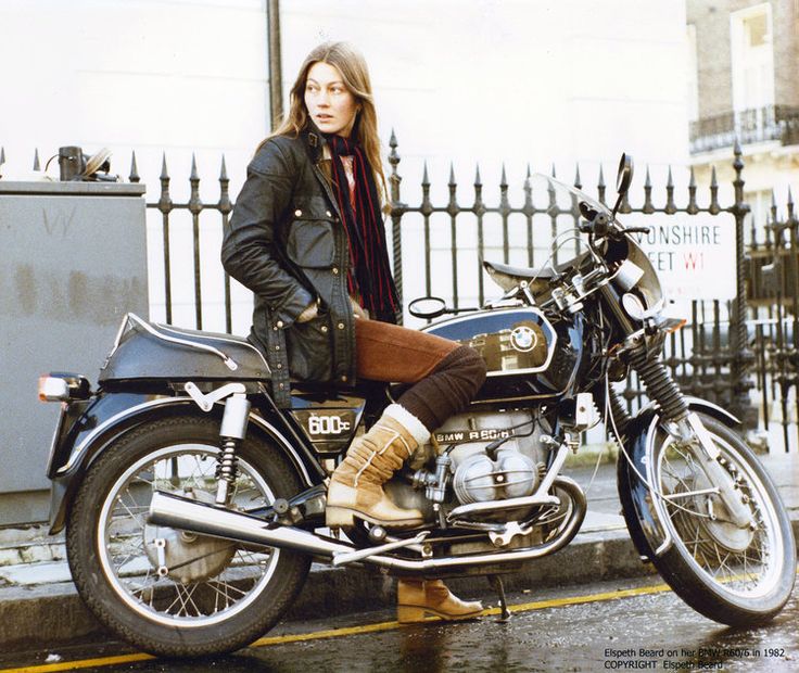 Woman in a black jacket sitting on a vintage BMW motorcycle, city street background, stylish and adventurous vibe.