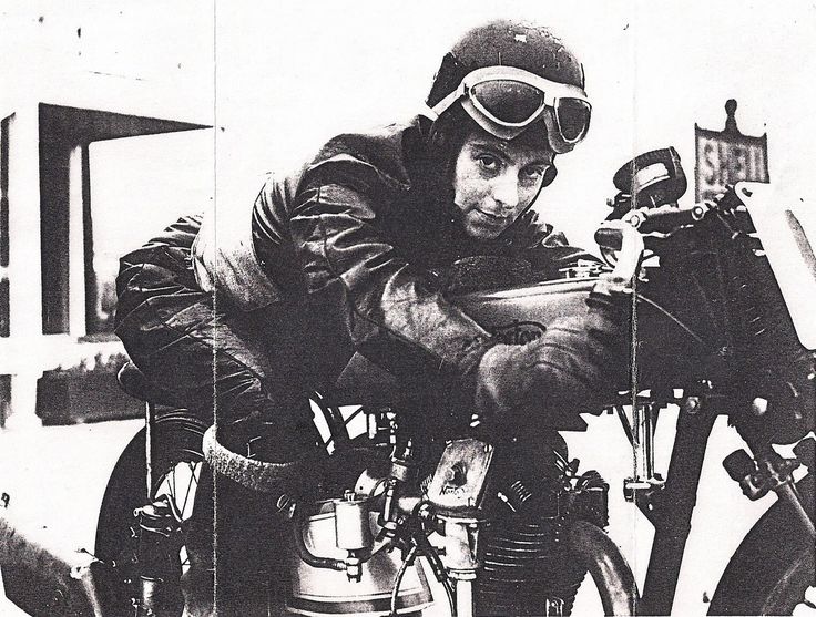 Vintage photo of a motorcyclist in leather gear and goggles, leaning forward on a classic racing motorcycle.