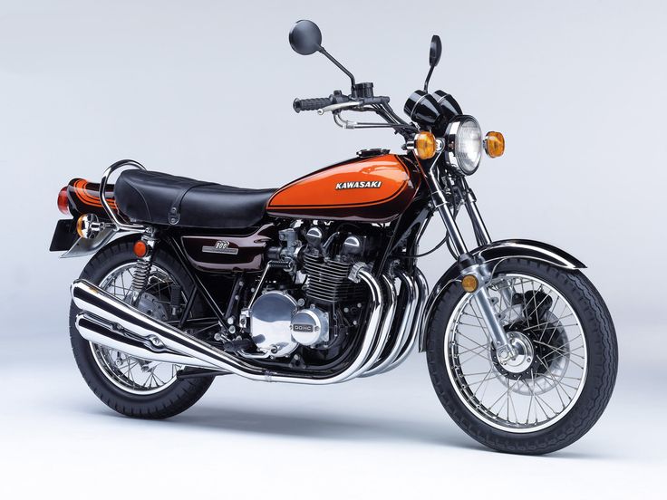 Vintage Kawasaki motorcycle with orange fuel tank, chrome exhaust, and classic styling, showcased in a studio setting.